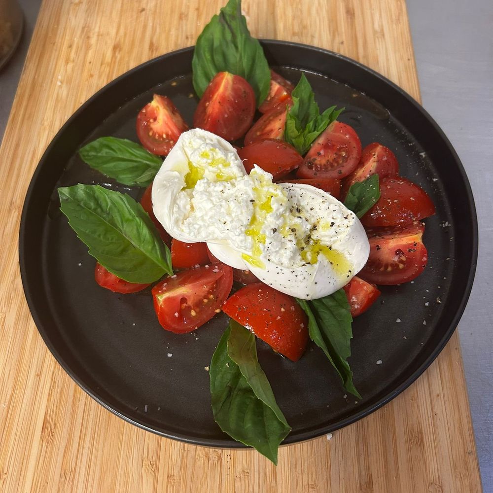 Sliced tomatoes, fresh basil and burrata drizzled with oil on a dark plate at Lilly's Italian Eatery