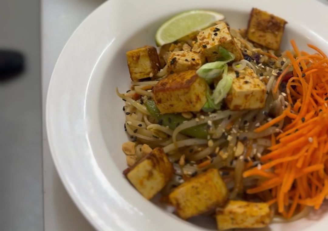 A tofu and rice noodle bowl with shredded carrots, green onion and a lime wedge at MegaMindful