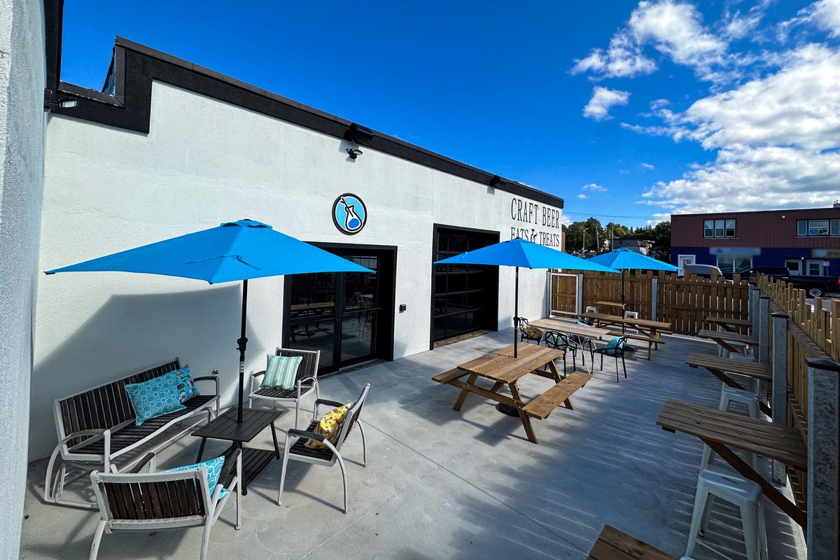 The patio at Test Batches Brewery with blue umbrellas, picnic tables and lounge chairs on a sunny day
